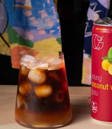 Café expreso helado con cubitos de hielo en un vaso, servido junto a una lata de agua de coco QF con yuzu.