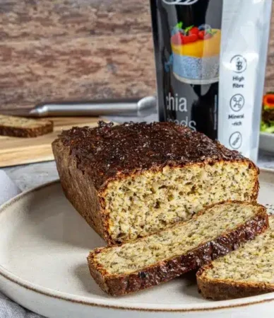 Un pain protéiné aux graines de chia et deux tranches de pain sur une assiette, disposés à côté d'un paquet de graines de chia Quality Food et de sandwichs au saumon.