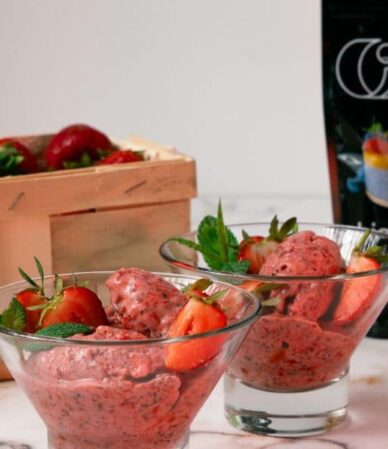 Truskawkowy sorbet proteinowy z chia w szklanych pucharkach, podany obok koszyka ze świeżymi truskawkami, puszki wody kokosowej QF i opakowania nasion chia.